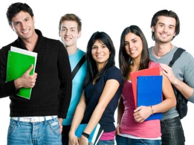 A group of five young adults stands together, smiling brightly. Each person holds colorful folders or notebooks, possibly filled with notes from their IB Tuition sessions. Casually dressed, they appear relaxed and cheerful against a white background.